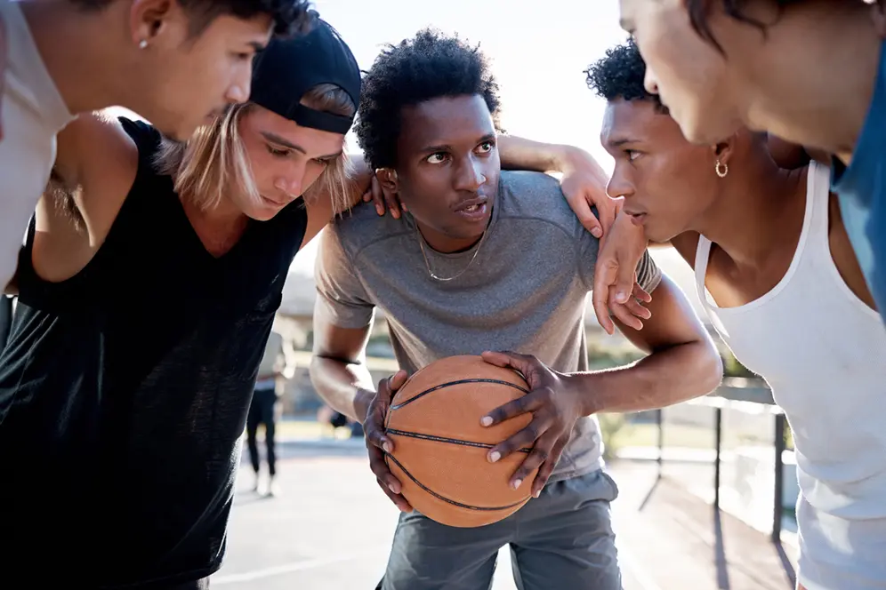cinq jeunes en tenue de sport se tenant regroupés autour d'un ballon de basket