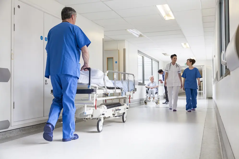 Agent du service public, brancardier poussant un lit médicalisé dans le couloir d'un centre de soin hospitalier.