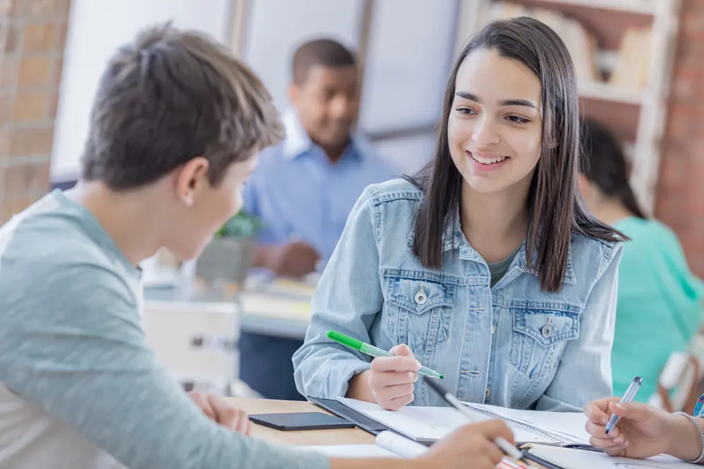 Un étudiant et une étudiante travaillent ensemble à une table, échangeant autour de leurs notes, dans une salle d’étude.