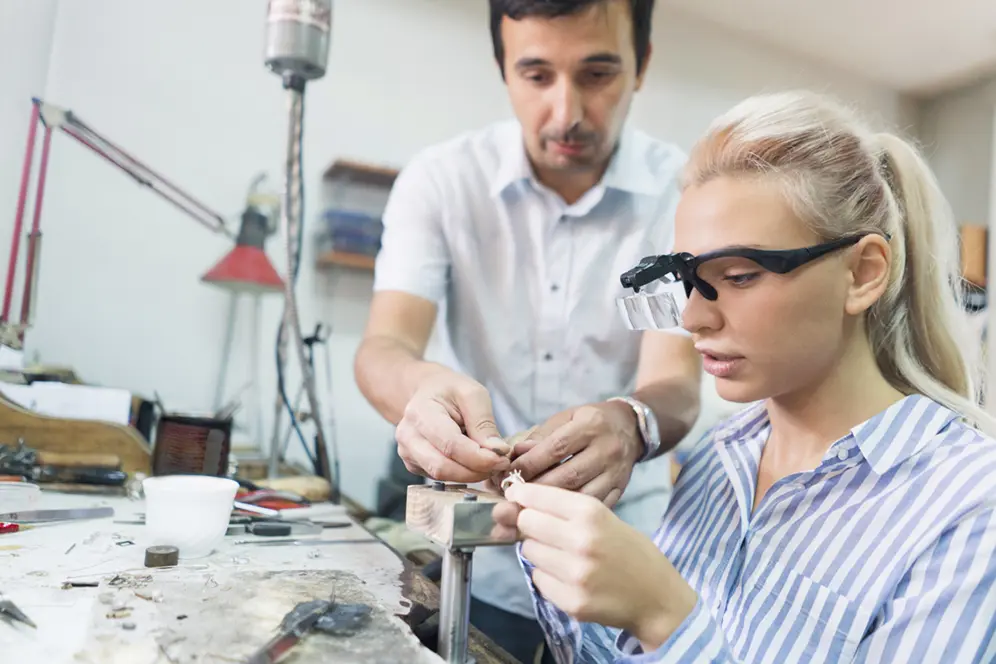 Une élève dans un atelier réalisant le sertissage d'une bague en collaboration avec un artisan joaillier.
