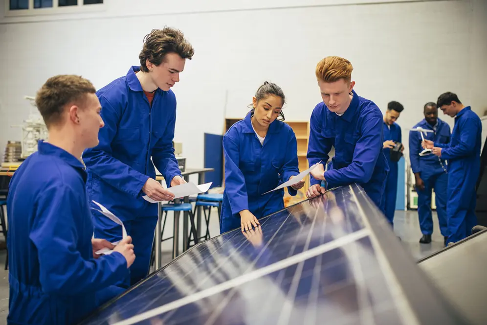 Trois garçons et une fille en bleu de travail en classe penchés sur des panneaux photovoltaïques