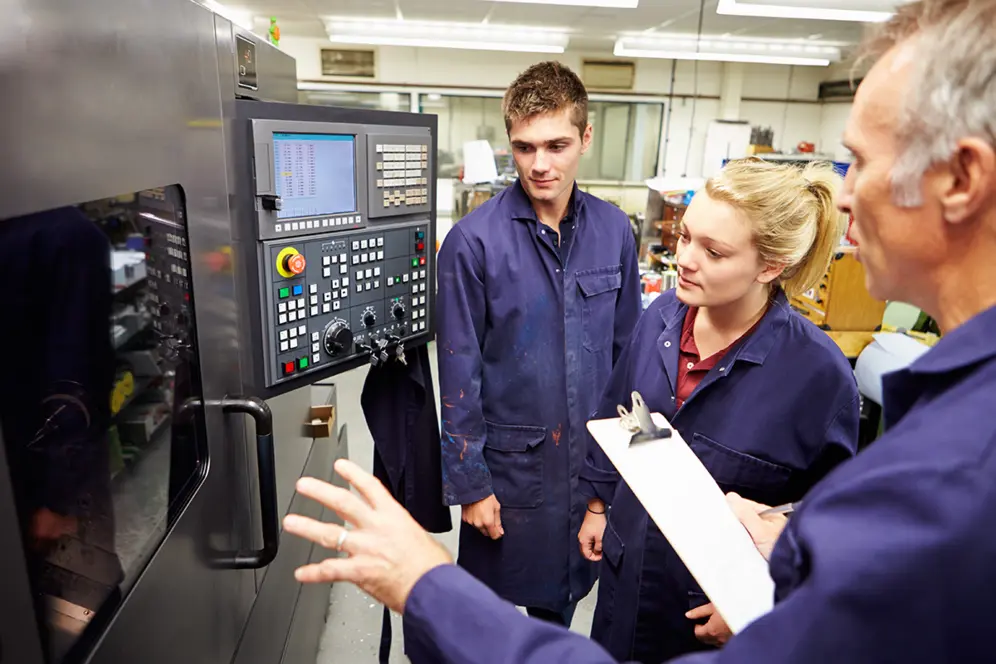 Des élèves de terminale pro échangent avec un formateur devant une machine industrielle dans l'atelier d'un lycée professionnel.