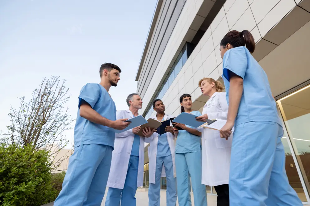 Étudiants en soins infirmiers en formation pratique lors d’un stage échangeant avec des personnels soignants devant un établissement de santé.