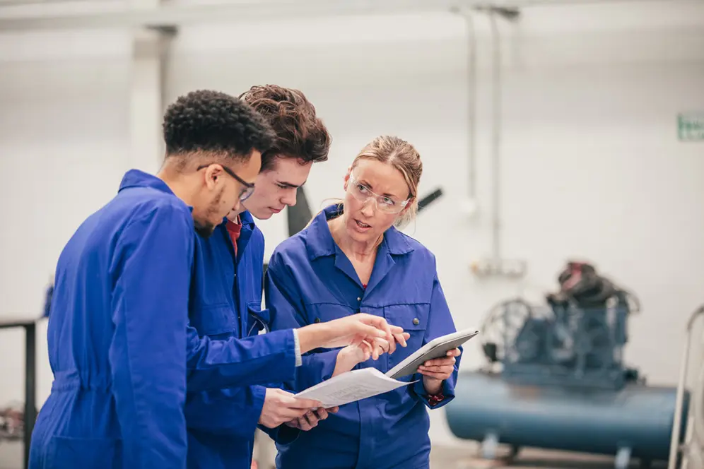 Un apprenti en formation collaborant avec un employé de l'entreprise, accompagné par une maîtresse d'apprentissage.