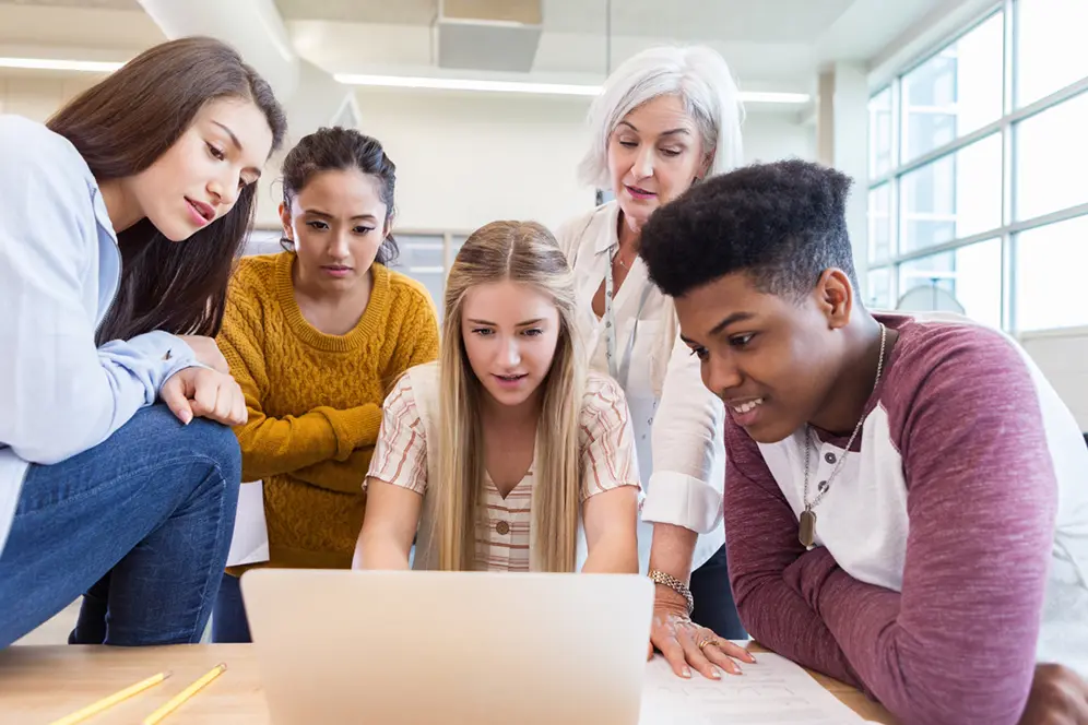 4 jeunes et une professeure regardent un écran d'ordinateur portable