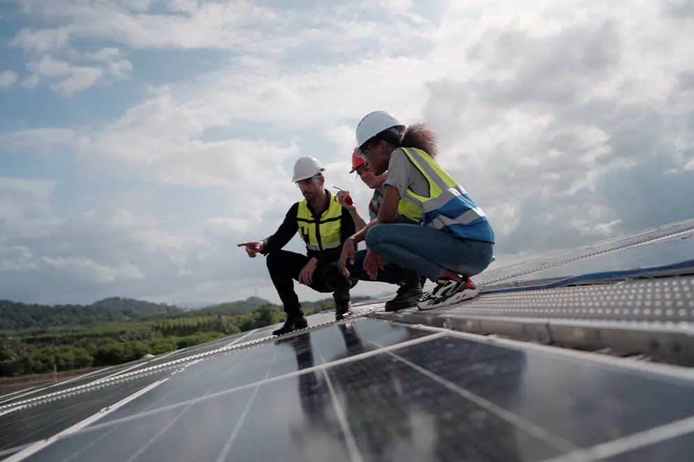 Trois personnes accroupies sur un toit compsé de panneaux solaires