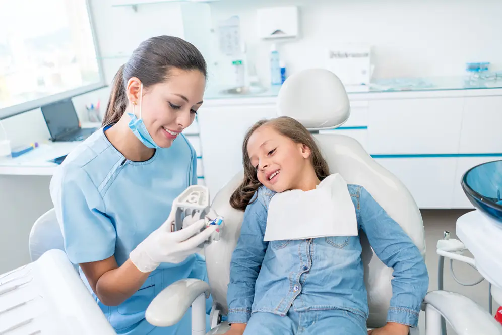 Femme dentiste montrant un modèle dentaire à une enfant allongée dans un fauteuil dans un cabinet.