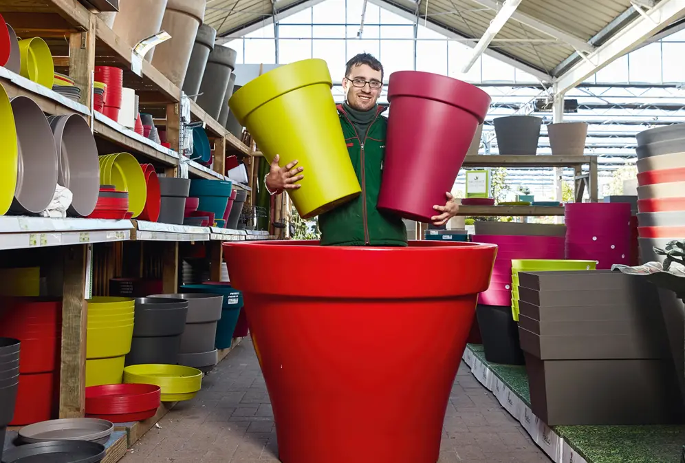 Jeune homme dans une jardinerie avec des gros pots de fleurs