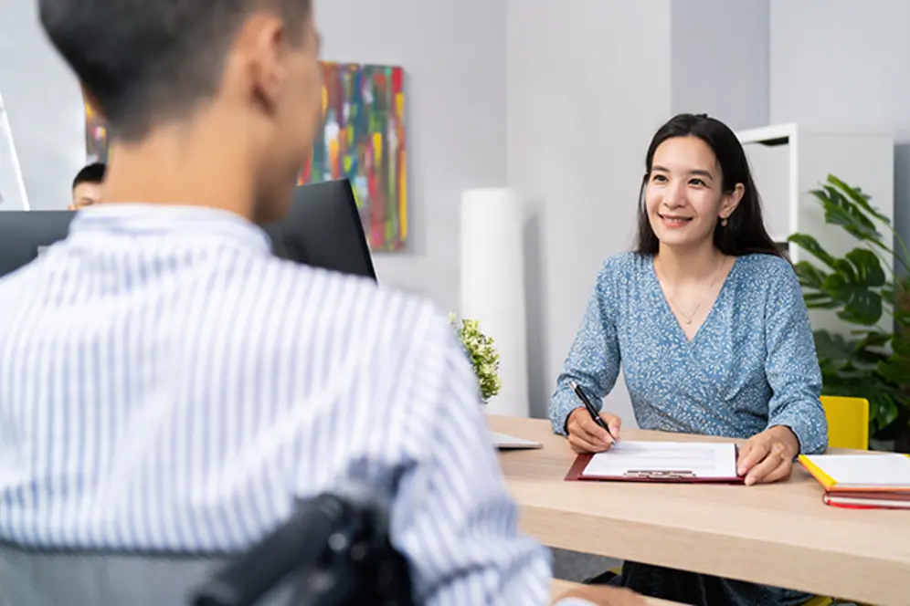 Un homme de dos et une femme de face assis en face à face dans un bureau, la femme prend des notes, illustrant un entretien ou un accompagnement professionnel.