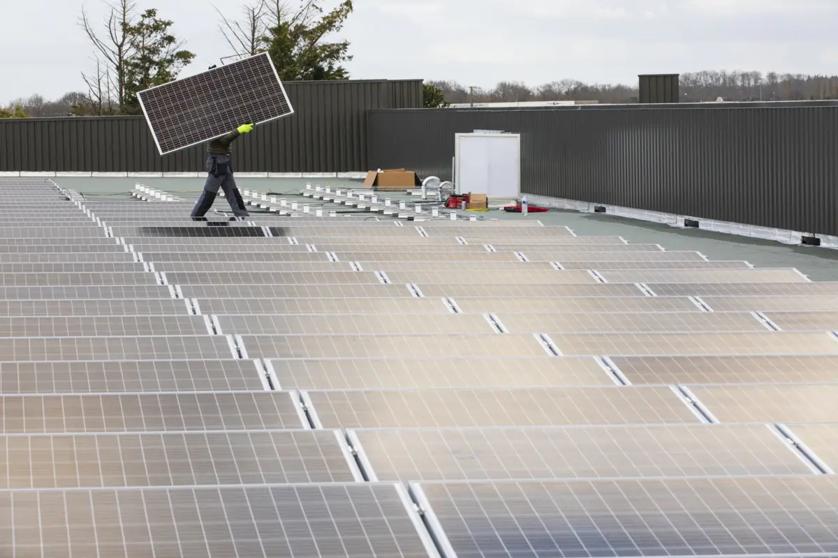 Un toit compos&eacute; de panneaux photovolta&iuml;ques. En arri&egrave;re plan quelqu'un porte un panneau.