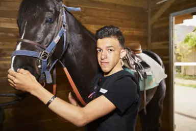 Pierre-Alfred caresse la t&ecirc;te d'un cheval dans son &eacute;curie