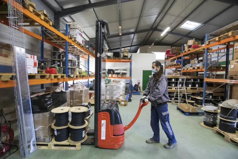 Dans un entrep&ocirc;t de mat&eacute;riel, l'assistante en conduite de projet manipule un transpalette rempli de bobines.