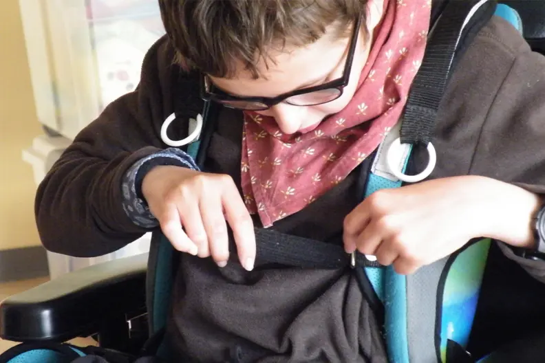 Alexandre manipule les sangles de son fauteuil roulant pour s'attacher dedans.