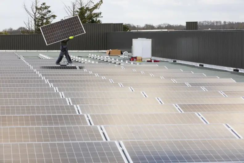 Un toit compos&eacute; de panneaux photovolta&iuml;ques. En arri&egrave;re plan quelqu'un porte un panneau.