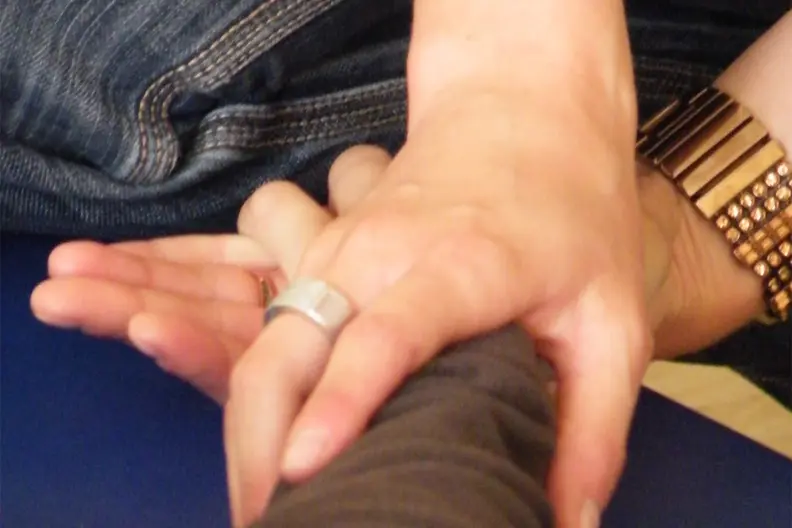 Gros plan sur des mains d'adultes qui manipulent une main et un bras d'enfant lors d'une s&eacute;ance de psychomotricit&eacute;.