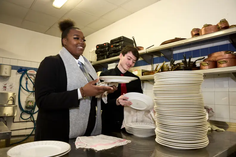 Deux &eacute;l&egrave;ves fille et gar&ccedil;on en restauration essuient des assiettes en cuisine.