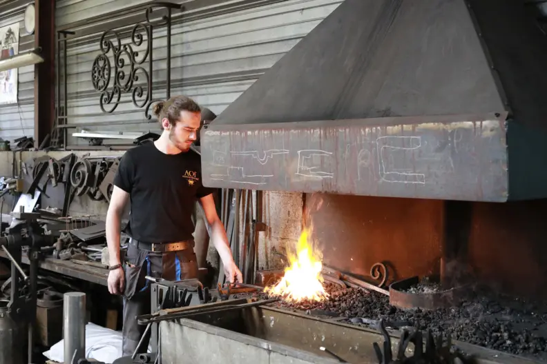 Le ferronnier devant une chemin&eacute;e, feu allum&eacute;, passe un objet au dessus de la flamme