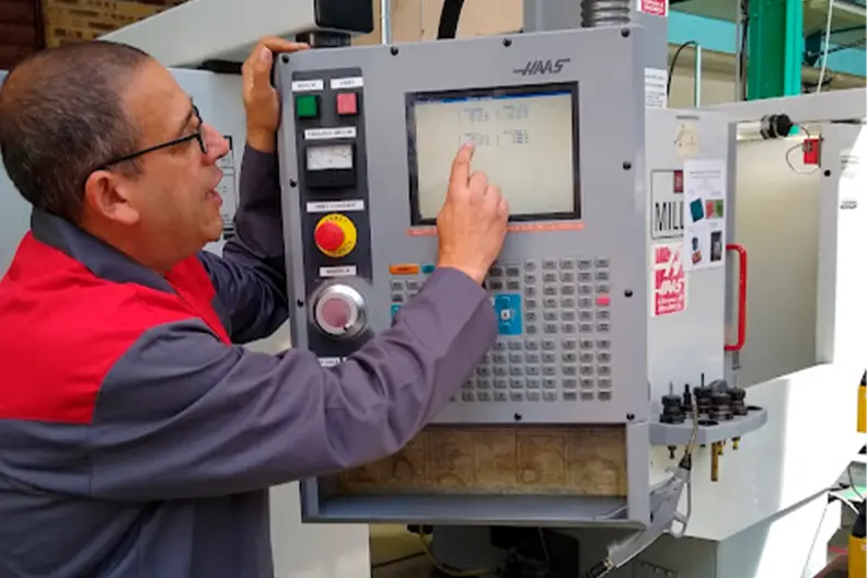 Un technicien d'usinage, le doigt pos&eacute; sur l'&eacute;cran d'une machine.