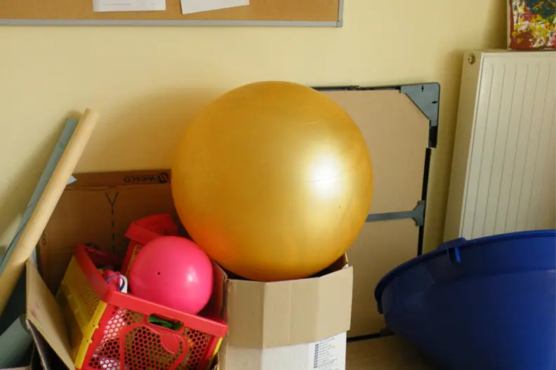 Empilement d'objets de psychomotricit&eacute;, comme des ballons, dans des cartons. Ils sont rang&eacute;s dans un coin.