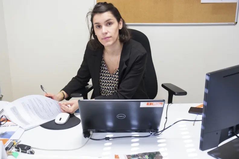 La responsable administrative travaille, assise derri&egrave;re son bureau, ordinateur portable ouvert.