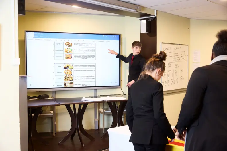 Un &eacute;l&egrave;ve en restauration fait d&eacute;filer un tableau de menus sur un grand &eacute;cran tactile.