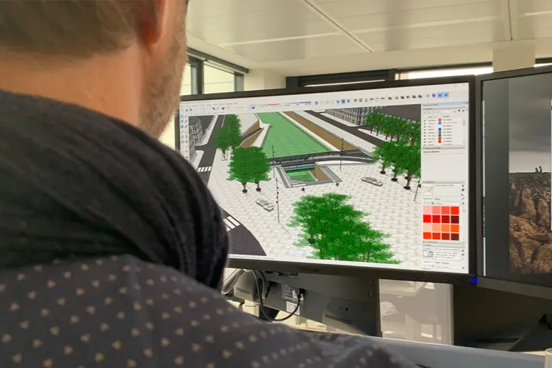 le dessinateur projeteur, de dos, regarde un &eacute;cran d'ordinateur. On y voir un plan virtuel d'un ext&eacute;rieur avec des arbres