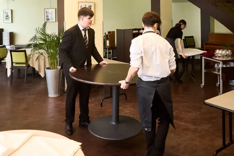 Deux &eacute;l&egrave;ves gar&ccedil;ons portent une table dans le restaurant du lyc&eacute;e.