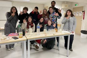 Un groupe de personnes pose dans une salle de cours autour de tables, en faisant le signe “je t’aime” en langue des signes.