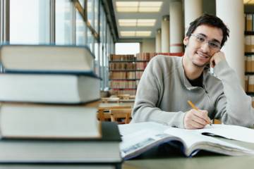Doctorant travaillant en bibliothèque pour préparer sa thèse dans le cadre d’un doctorat au sein d’une école doctorale.