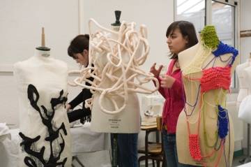 Deux jeunes filles travaillent sur des mannequins habillés de créations textiles expérimentales, dans un atelier de mode.